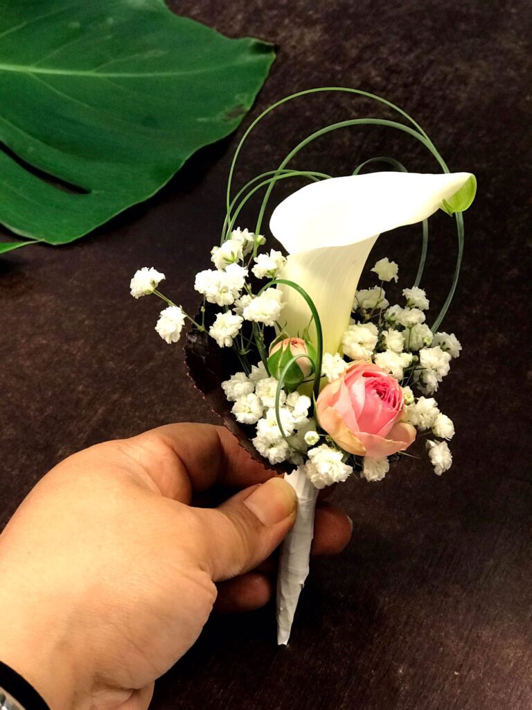 Boutonnière de mariage élégante avec un petit arum blanc, une rose rose pâle et du gypsophile — Gladys Fleurs Bruxelles