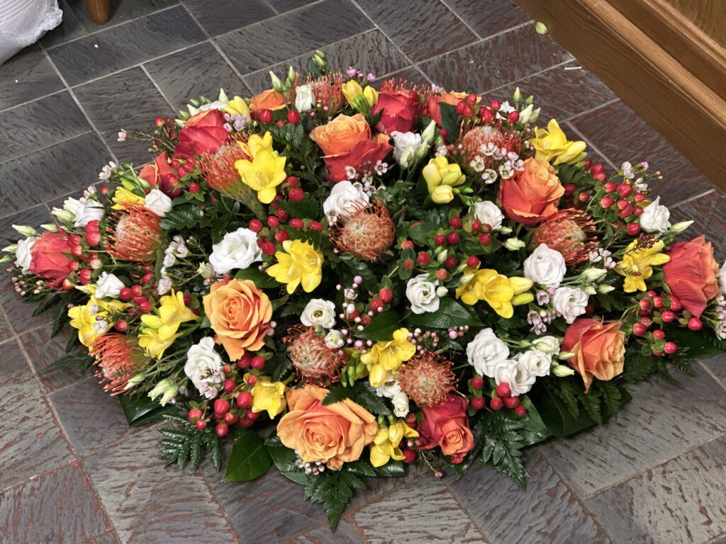 Coussin funerailles compos&eacute; de roses orange, freesias jaunes, lysianthus blancs et prot&eacute;as exotiques &mdash; Gladys Fleurs Bruxelles